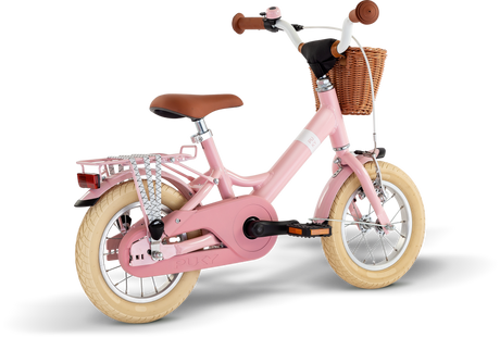 PUKY Barncykel Youke 12 Classic är en charmig 12" rosa cykel för barn i åldrarna 3 år, med krämfärgade däck, brunt styre, en flätad korg, bakre bagagehylla, träningshjul och ett kedjeskydd för säkerheten.