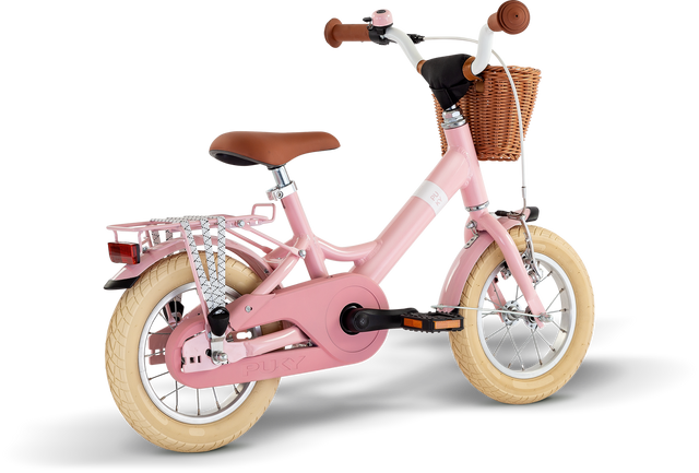 PUKY Barncykel Youke 12 Classic är en charmig 12" rosa cykel för barn i åldrarna 3 år, med krämfärgade däck, brunt styre, en flätad korg, bakre bagagehylla, träningshjul och ett kedjeskydd för säkerheten.