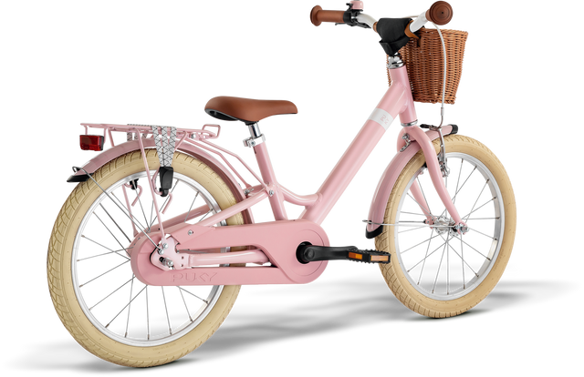 PUKY Barncykel 18" för barn i 5-årsåldern har en rosa ram, vita däck, en brun lädersadel och handtag, en flätad korg framtill och ett bakre metallställ. Designen PUKY YOUKE 18 Classic inkluderar ett kedjeskydd och lättviktskomponenter för enkel körning.