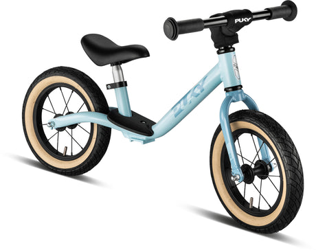 En ljusblå Balanscykel - Lufthjul - Puky LR Light med svart styre, svart säte, och beiga Lufthjul-däck. Cykeln har inga pedaler och är designad för att små barn ska lära sig balans. Märket "PUKY" visas på ramen och styret.
