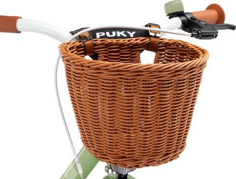 Närbild av ett cykelstyre med en PUKY Cykelkorg för 16" & 18" cyklar, fäst med läderremmar. De bruna handtagen och en bromsspak på höger sida är synliga, perfekt för alla dina barncyklaräventyr.