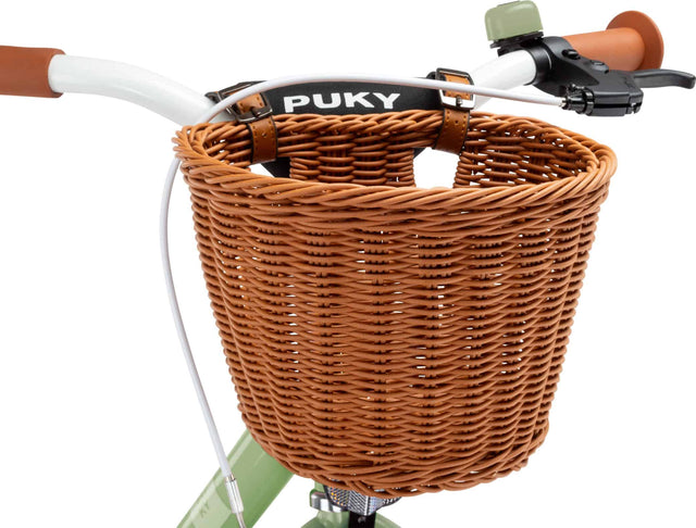 Närbild av ett cykelstyre med en PUKY Cykelkorg för 16" & 18" cyklar, fäst med läderremmar. De bruna handtagen och en bromsspak på höger sida är synliga, perfekt för alla dina barncyklaräventyr.