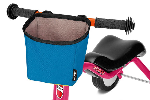 Närbild av en rosa balanscykel för barn, liknande stilen som Wutsch-serien, med en blå tygkorg på styret. Den är utrustad med en svart sits och texturerade svarta grepp. PUKY-märkeslogotypen är synlig på både ramen, besläktad med Pukylino-designen, och Styrväska för Pukylino, Wutsch, Fitsch, Pukymoto - Puky LT 3-korgen.